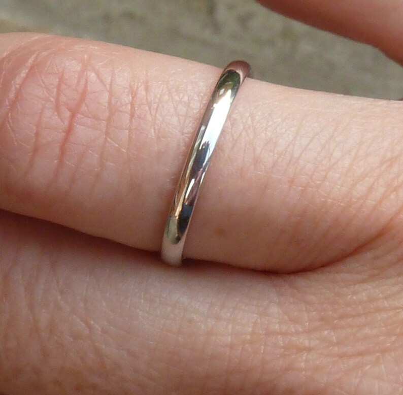 Puede incluir: Un anillo de banda de plata simple usado en un dedo.