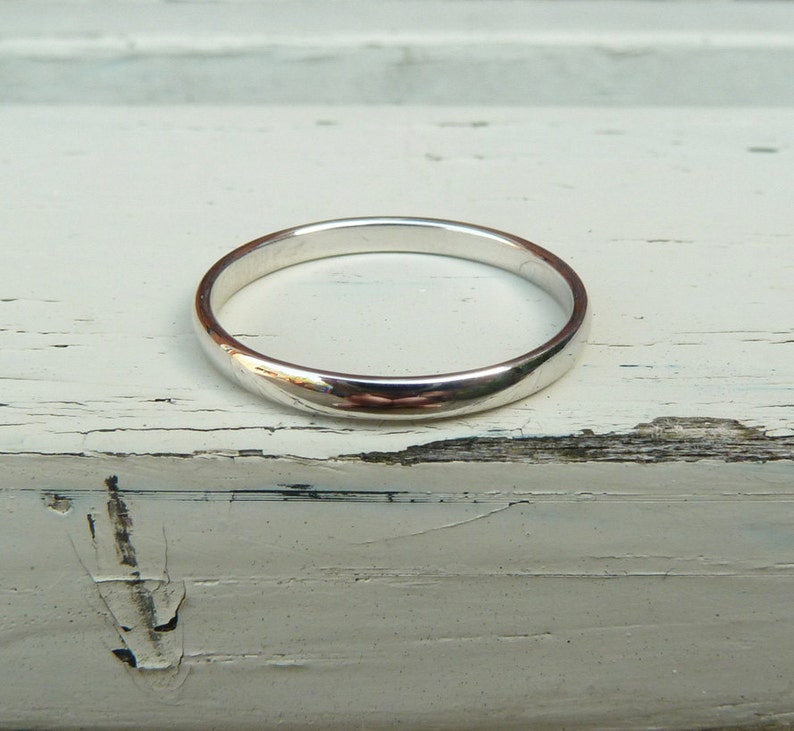Puede incluir: Un anillo de banda de plata simple, mostrado sobre una superficie de madera blanca.