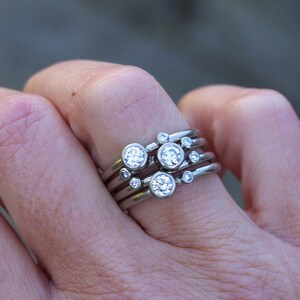 May include: A set of five silver rings with small round diamonds. The rings are stacked on each other and are worn on a finger.