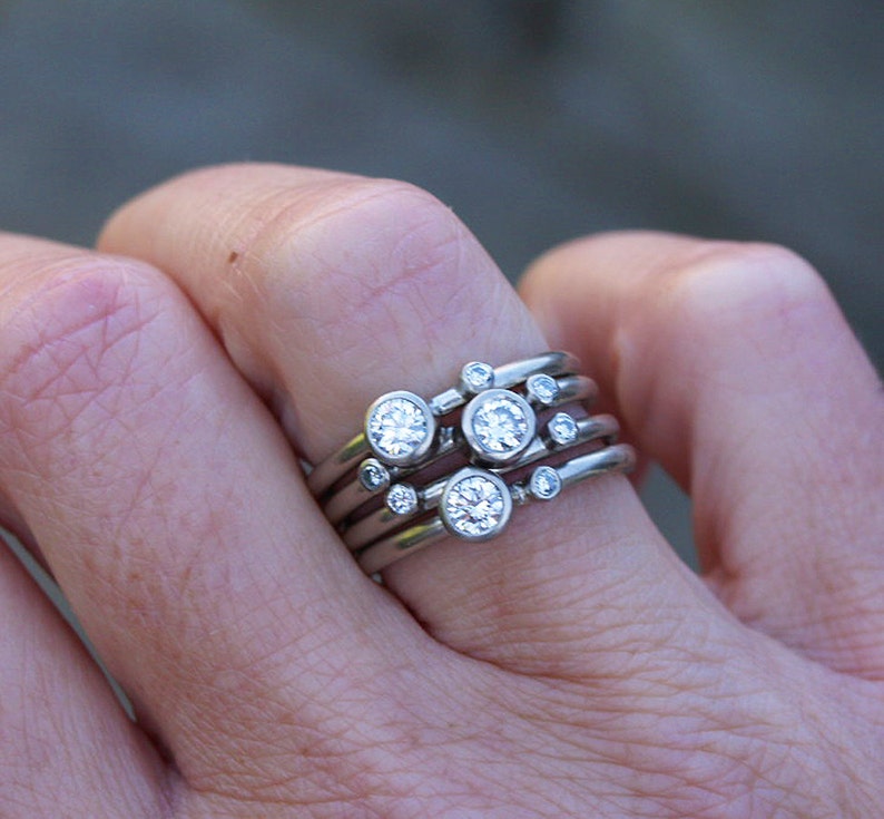 May include: A set of five silver rings with small round diamonds. The rings are stacked on each other and are worn on a finger.