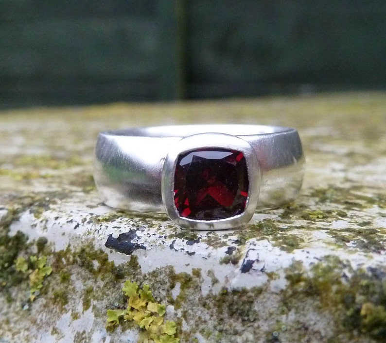 May include: A silver ring with a square-shaped red gemstone set in a bezel setting.
