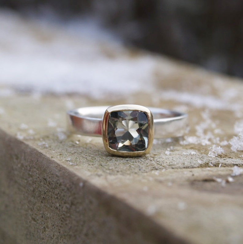 Puede incluir: Un anillo de plata y oro con una piedra preciosa verde de forma cuadrada.