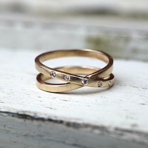 May include: A gold band ring with a criss-cross design and small diamonds set into the band.