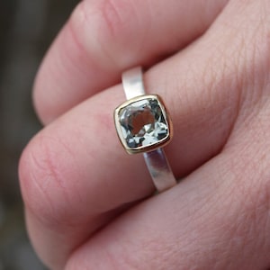 Puede incluir: Un anillo de plata con una banda de oro y una piedra preciosa cuadrada de color verde claro.