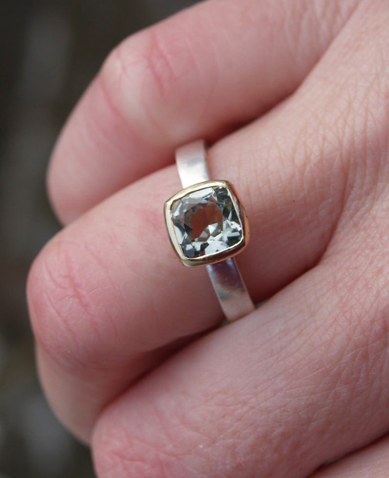 Puede incluir: Un anillo de plata con una banda de oro y una piedra preciosa cuadrada de color verde claro.