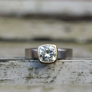 May include: A square-shaped diamond ring with a gold setting and a silver band.