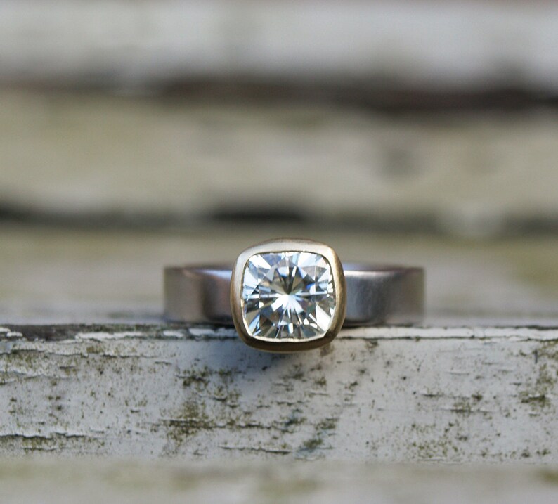 May include: A square-shaped diamond ring with a gold setting and a silver band.