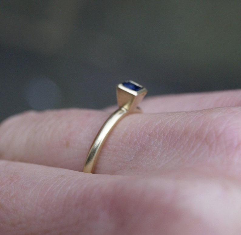 May include: A gold ring with a small, dark blue gemstone set in a square shape.