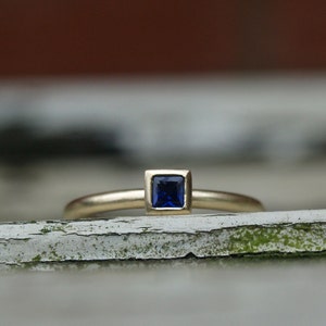 May include: A gold ring with a square-shaped blue gemstone set in a gold bezel.