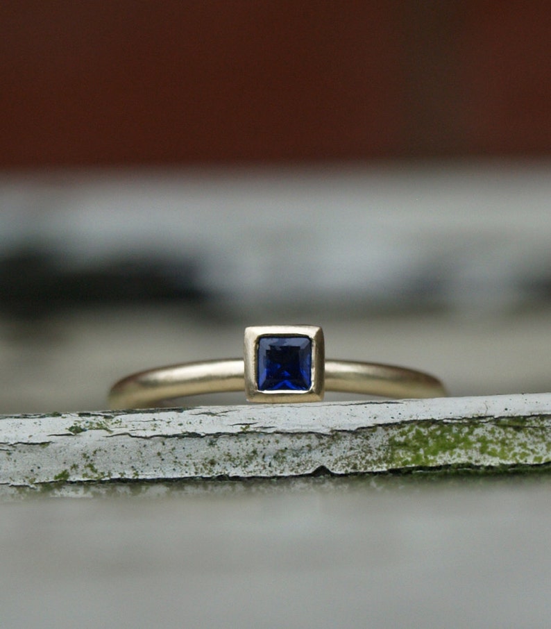May include: A gold ring with a square-shaped blue gemstone set in a gold bezel.