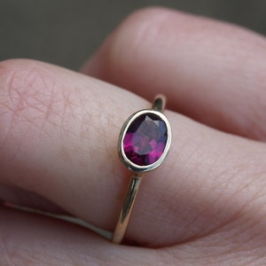 May include: A gold ring with a deep purple oval gemstone set in a bezel setting.