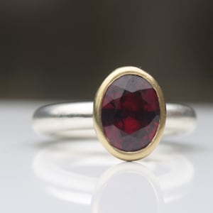 May include: A silver ring with a red gemstone set in a gold bezel.