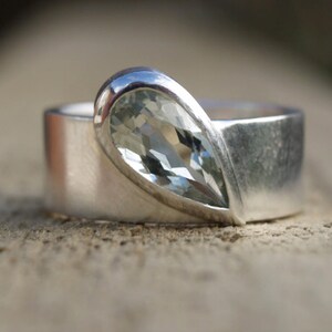 May include: A silver ring with a pear-shaped clear gemstone set in a silver band.