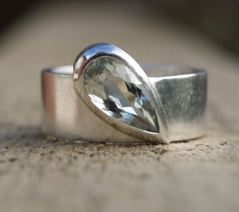 May include: A silver ring with a pear-shaped clear gemstone set in a silver band.
