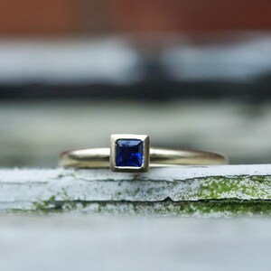 May include: A gold ring with a square-shaped blue sapphire gemstone.