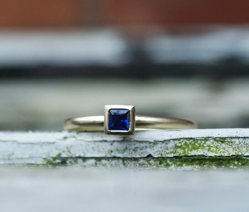 May include: A gold ring with a square-shaped blue sapphire gemstone.