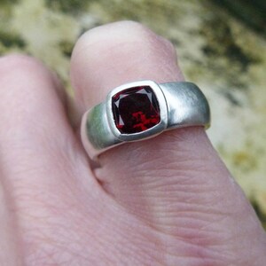 May include: A silver ring with a square red gemstone set in a bezel setting.