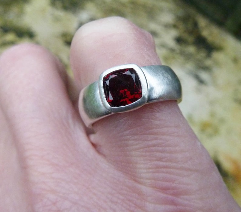 May include: A silver ring with a square red gemstone set in a bezel setting.