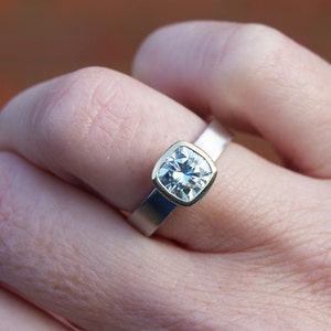 May include: A silver and gold ring with a large, square-shaped, clear gemstone.