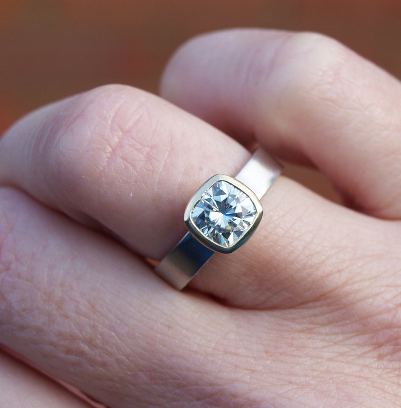 May include: A silver and gold ring with a large, square-shaped, clear gemstone.