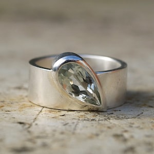 May include: A silver ring with a pear-shaped green gemstone set in the band.