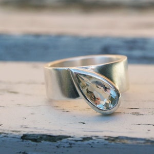 May include: A silver ring with a teardrop-shaped clear gemstone set in the band.