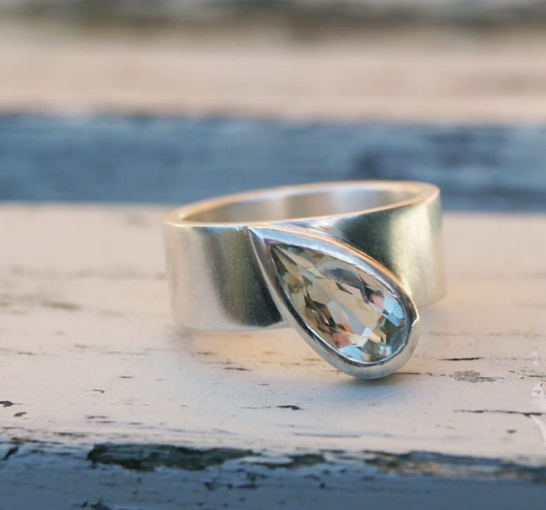 May include: A silver ring with a teardrop-shaped clear gemstone set in the band.