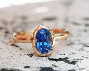 May include: A gold ring with a bezel setting featuring a large oval blue sapphire gemstone.