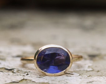 May include: A gold ring featuring a large, oval-shaped, dark blue gemstone.