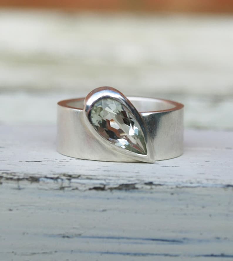 May include: A silver ring with a pear-shaped clear gemstone set in the band.