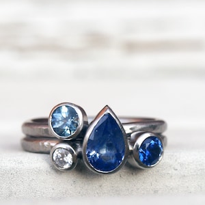 Könnte beinhalten: Mehrere silberne Ringe mit blauen Edelsteinen. Die Ringe haben einen tropfenförmigen Saphir, einen runden hellblauen Edelstein, einen kleinen weißen Edelstein und einen runden dunkelblauen Edelstein.