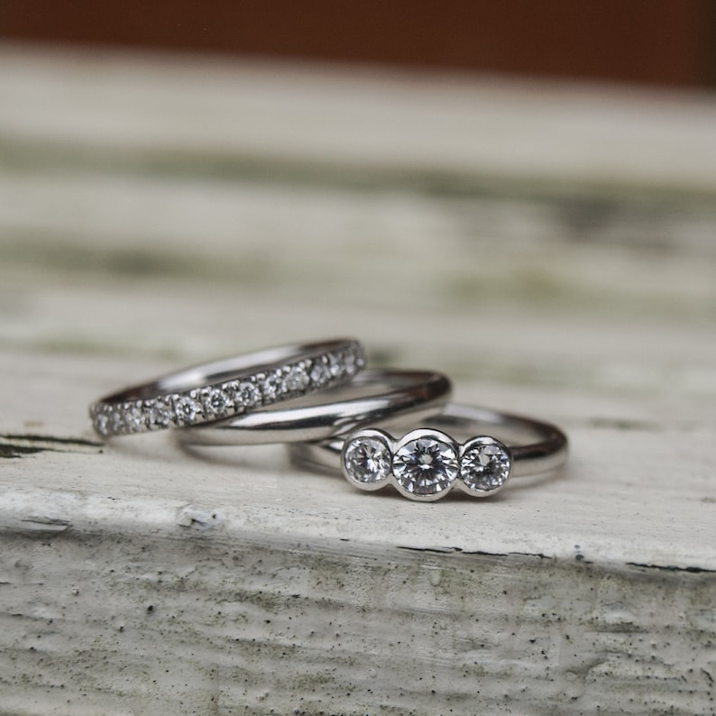 Pode incluir: Tr&ecirc;s an&eacute;is de prata com diamantes. O anel superior tem tr&ecirc;s diamantes redondos em fila. O anel do meio &eacute; uma banda lisa. O anel inferior tem uma fila de diamantes pequenos.
