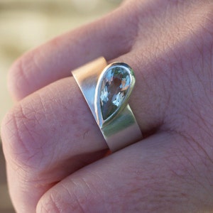 May include: A silver ring with a pear-shaped light green gemstone set in the center.