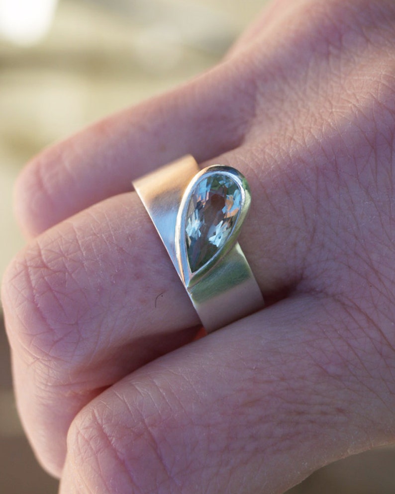 May include: A silver ring with a pear-shaped light green gemstone set in the center.