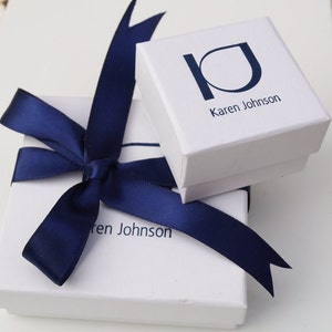 Pode incluir: Duas caixas de presente brancas com la&ccedil;os de fita azul marinho. A caixa superior tem o texto "Karen Johnson" impresso. A caixa inferior tem o texto "ren Johnson" impresso.