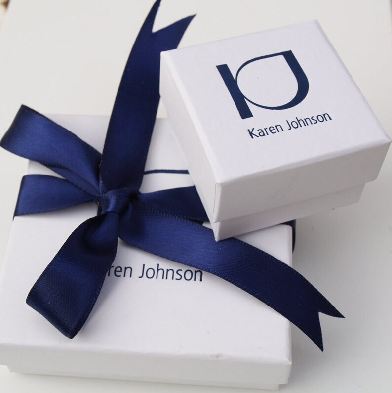 Pode incluir: Duas caixas de presente brancas com la&ccedil;os de fita azul marinho. A caixa superior tem o texto "Karen Johnson" impresso. A caixa inferior tem o texto "ren Johnson" impresso.