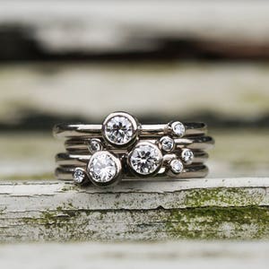 May include: A set of five silver rings with small round diamonds set in each band. The rings are stacked on top of each other, creating a cluster of diamonds.