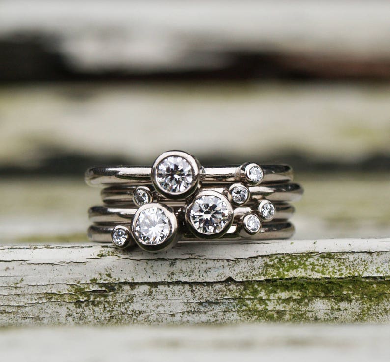 May include: A set of five silver rings with small round diamonds set in each band. The rings are stacked on top of each other, creating a cluster of diamonds.