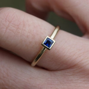May include: A gold ring with a square blue sapphire gemstone.