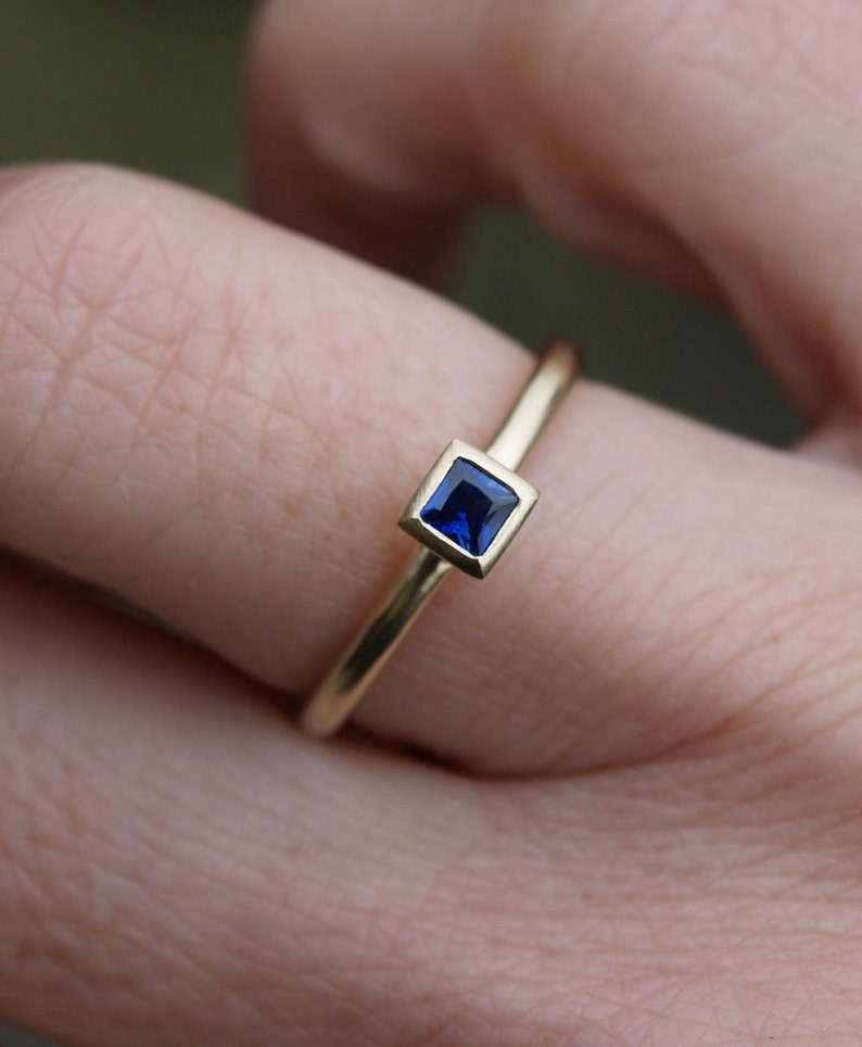 May include: A gold ring with a square blue sapphire gemstone.