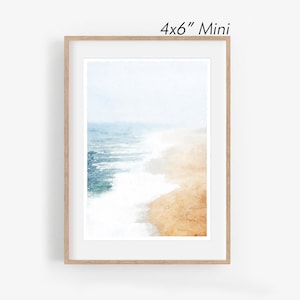 May include: A framed watercolor print of a beach scene. The artwork depicts the ocean meeting the sand, with shades of blue, white, and tan. The frame is a light wood color, and the text "4x6" Mini" is visible at the top.