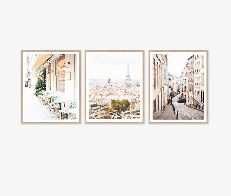Paris Prints Digital Printable Set of 3, Paris France Cafe, Cityscape Streets Buildings Architecture, Neutral French Decor 5x7, 8x10, 11x14 . A set of three watercolor-style prints depicting scenes from Paris. The first print shows a cafe with tables and chairs on a sidewalk. The second print shows a view of the city with the Eiffel Tower in the distance. The third print shows a narrow street lined with buildings.