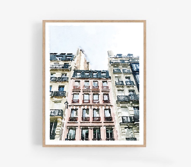 Puede incluir: Una pintura de acuarela de una fila de edificios parisinos con un edificio rosa en el centro. Los edificios tienen muchas ventanas y balcones. El cielo es azul claro con nubes blancas.