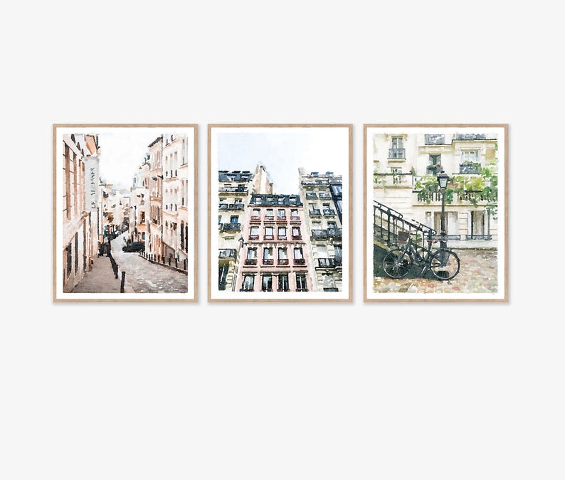 Paris Art Prints Digital Download Wall Art Set of 3, Paris Photography, Neutral Art, Paris Wall Decor, France Buildings Streets Watercolor. A set of three watercolor paintings depicting Parisian streets. The first painting shows a narrow street with buildings on both sides. The second painting shows a close-up of a building with windows and balconies. The third painting shows a bicycle parked on a cobblestone street with a lamppost and greenery in the background.