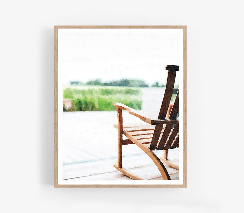 May include: A watercolour painting of a wooden rocking chair on a porch. The chair is made of light-coloured wood with a dark brown backrest. The background features a blurred green field and a bright sky, creating a serene outdoor scene.