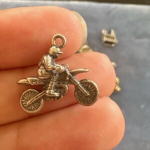 Peut inclure: Charme en argent d'un pilote de motocross sur une moto tout-terrain. Le charme a une boucle en haut pour l'attacher &agrave; un bracelet ou un collier.