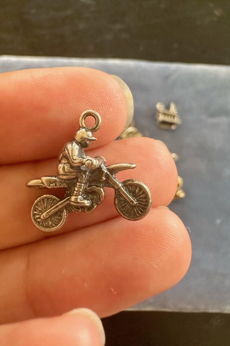 Peut inclure: Charme en argent d'un pilote de motocross sur une moto tout-terrain. Le charme a une boucle en haut pour l'attacher &agrave; un bracelet ou un collier.