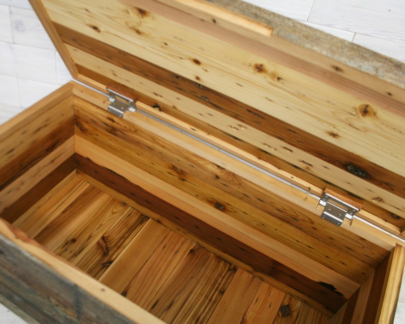 Puede incluir: Un cofre de almacenamiento de madera con tapa con bisagras, hecho de madera recuperada con una variedad de tonos y texturas de madera. El cofre est&aacute; abierto, revelando el interior, que tambi&eacute;n est&aacute; hecho de madera recuperada.