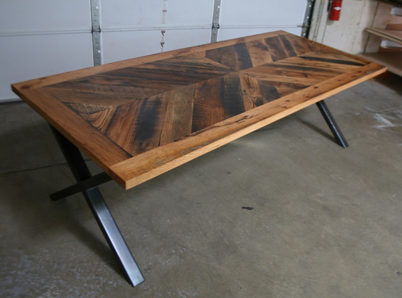 Pu&ograve; includere: Un tavolo da pranzo in legno rustico con un piano a motivo chevron e gambe a X in metallo nero.