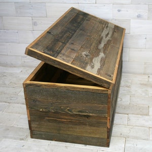 Puede incluir: Un cofre de almacenamiento de madera con tapa con bisagras, hecho de tablones de madera recuperados con un acabado r&uacute;stico. La tapa est&aacute; abierta, revelando el interior del cofre.